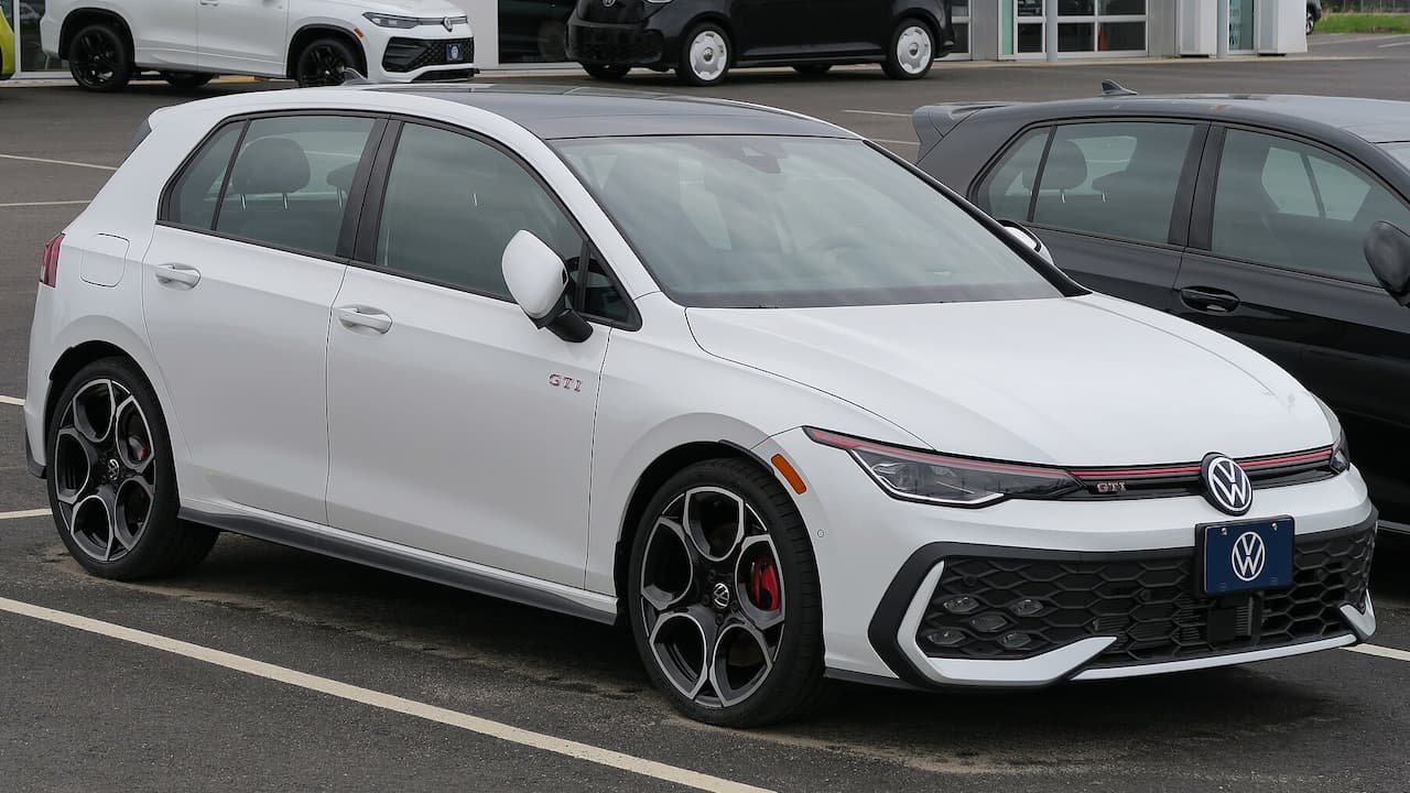 White 2025 Volkswagen GTI with red brake calipers and distinctive alloy wheels parked in dealership lot