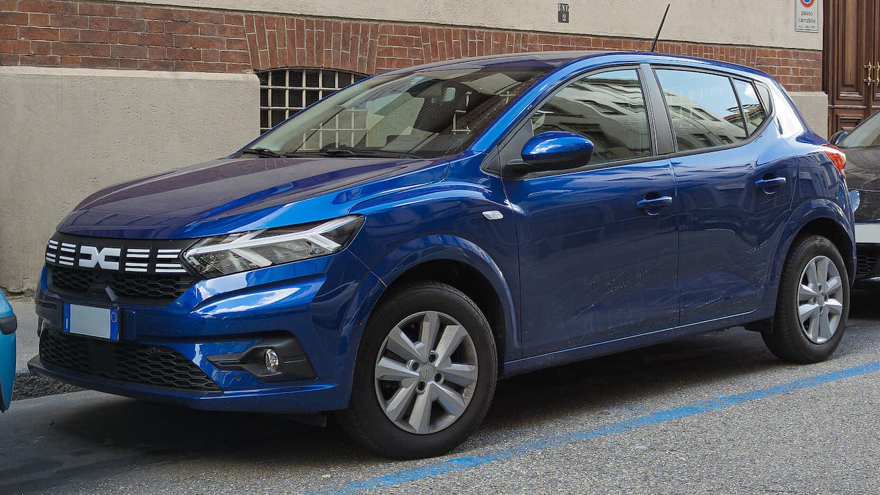 Blue Dacia Sandero parked on street with blue parking lines, featuring distinctive front grille and silver alloy wheels