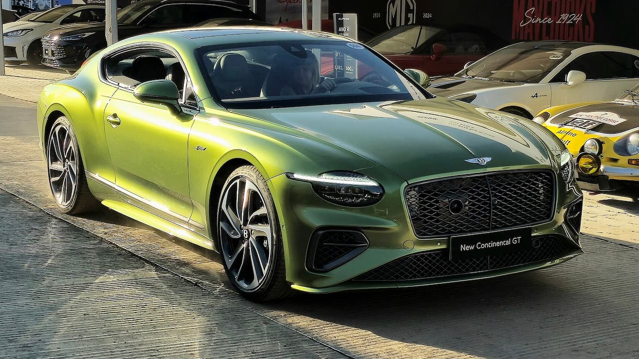 Green Bentley Continental GT Speed parked on brick pavement at car show with other luxury vehicles in background