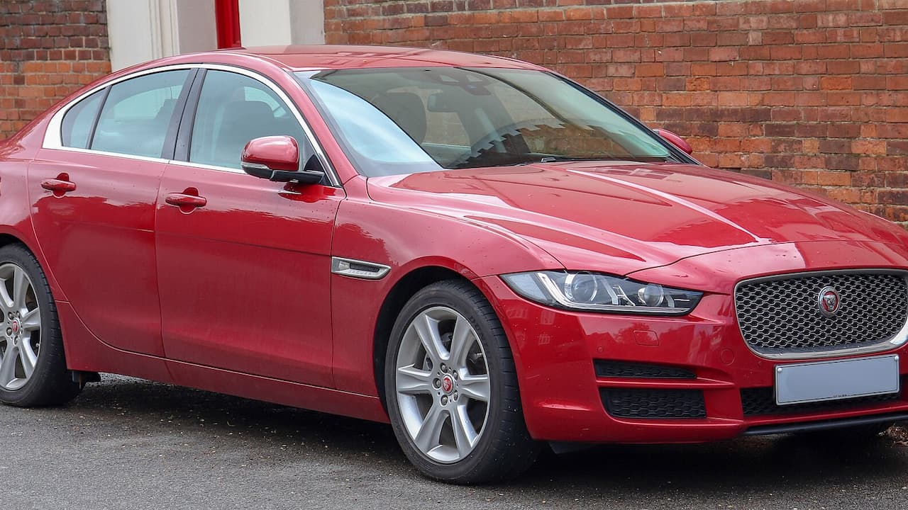 Red 2025 Jaguar XE parked beside brick wall with distinctive mesh grille and sleek LED headlights