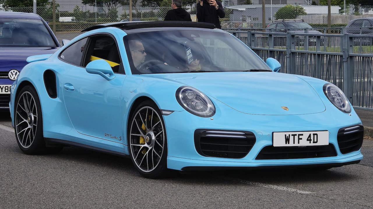 Light blue Porsche 911 Turbo S with distinctive side air intakes and sport wheels parked with driver visible inside