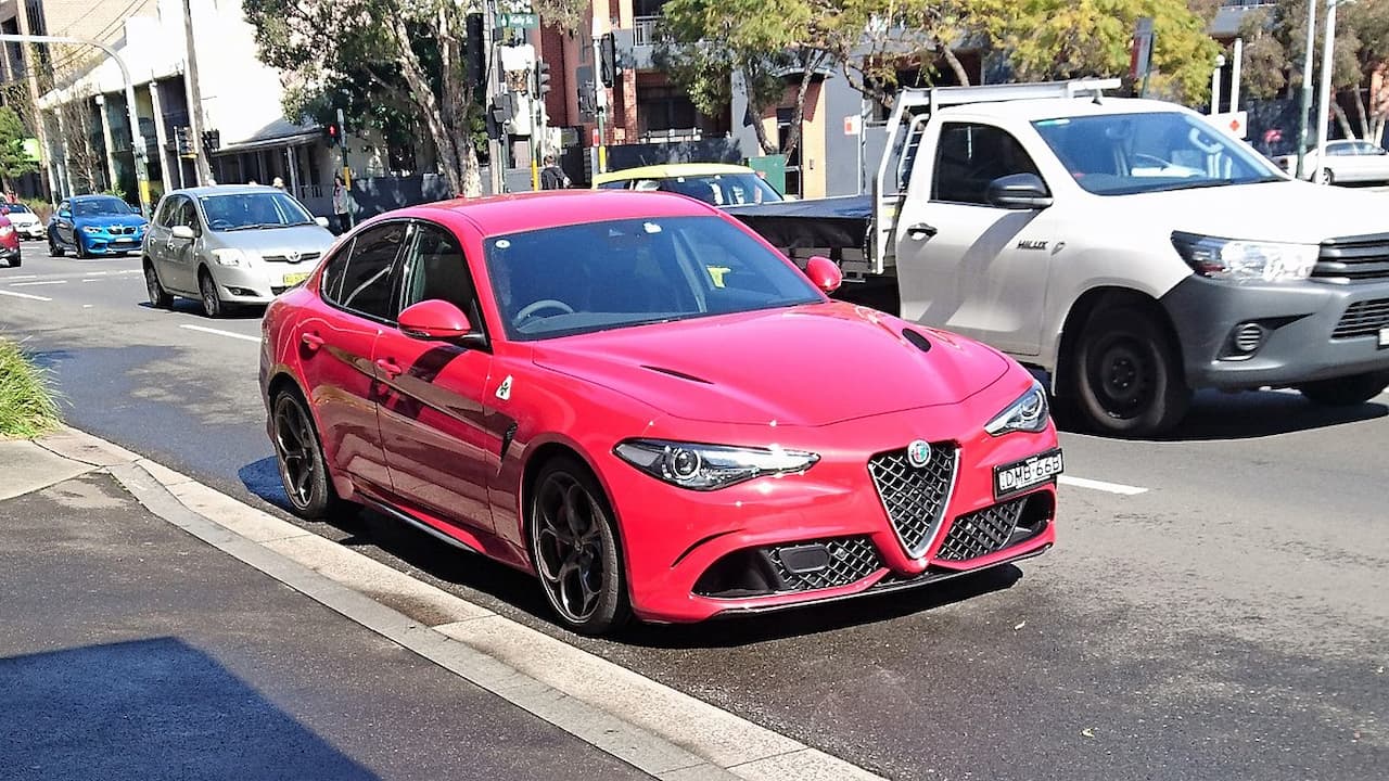 Red Alfa Romeo Giulia Quadrifoglio with distinctive triangular grille and cloverleaf badge parked on busy urban street