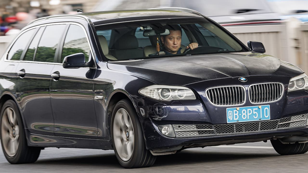 Black BMW 5 Series Touring in motion with driver visible, featuring kidney grille and blue license plate on street