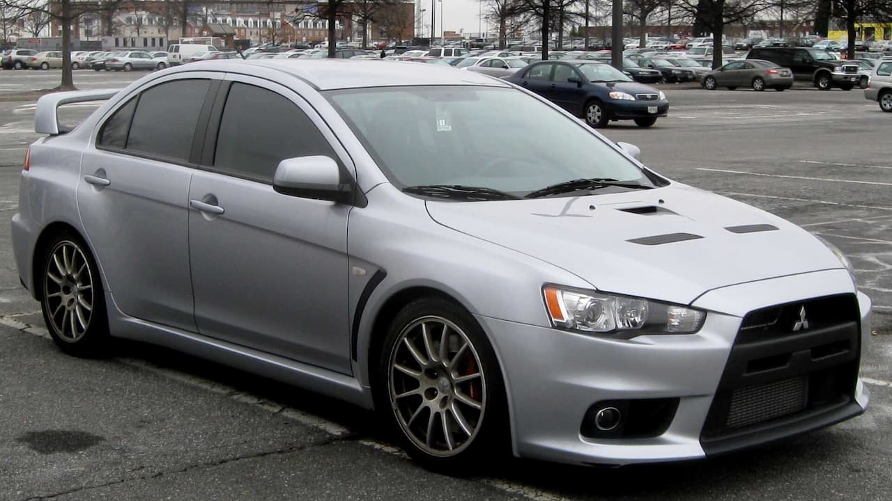 Silver Mitsubishi Lancer Evolution X parked in parking lot with hood vents and multi-spoke alloy wheels visible