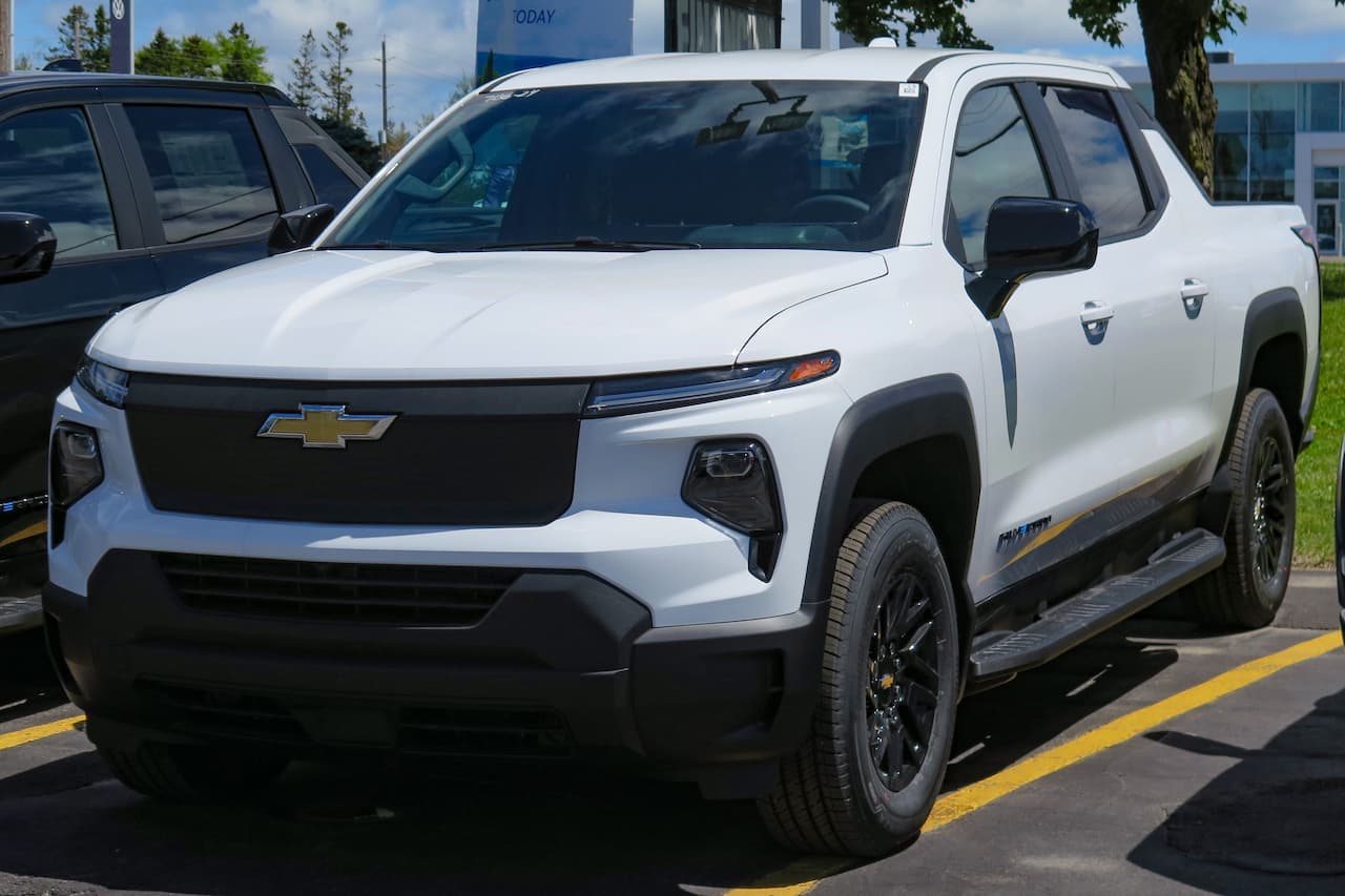 White Chevrolet Silverado EV RST electric pickup truck parked at dealership with black grille, LED headlights, and black wheels