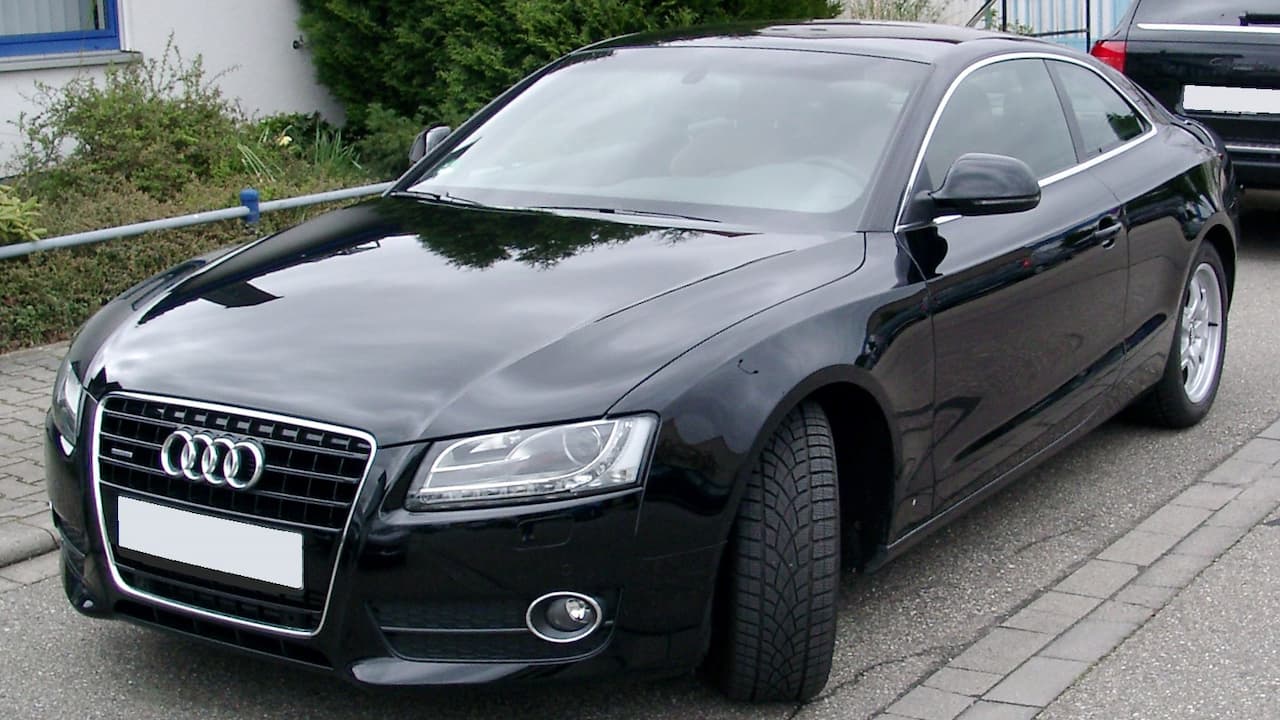 Black Audi A5 parked on cobblestone street with LED headlights, chrome grille, and fog lights in residential area