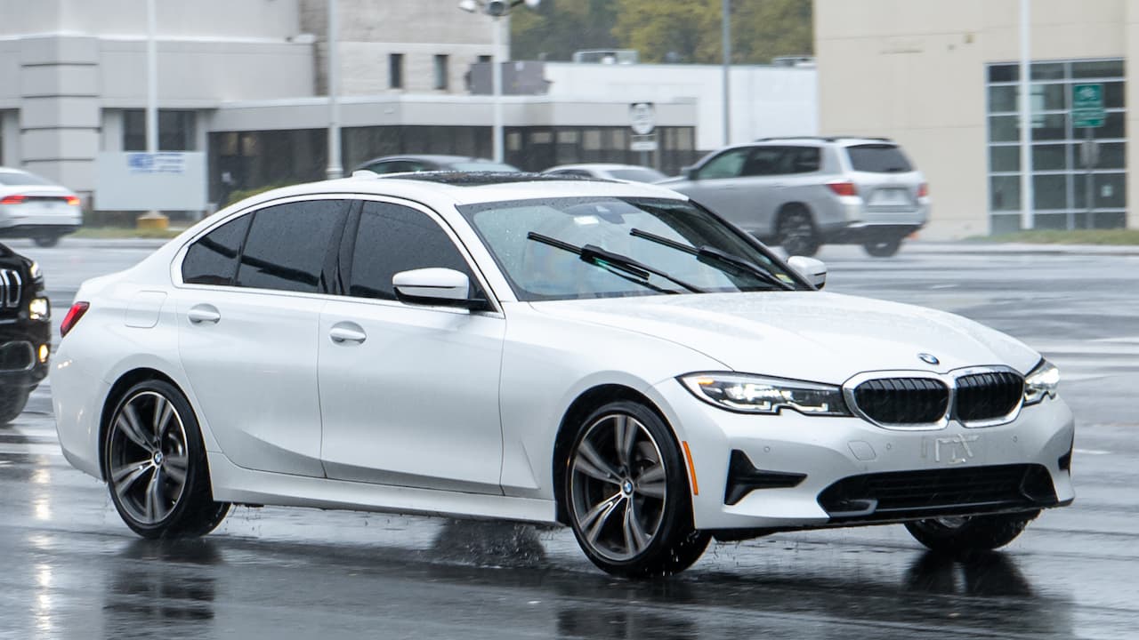 White BMW 330i G20 with kidney grille and sport wheels parked on wet pavement in modern urban setting