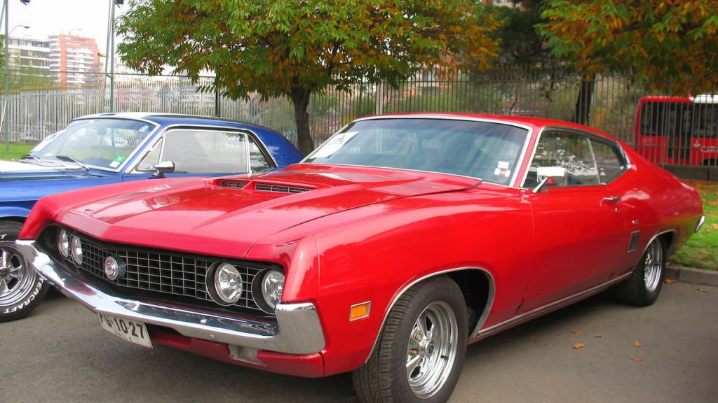 Red 1970 Ford Torino GT classic muscle car parked at car show with blue vehicle beside it