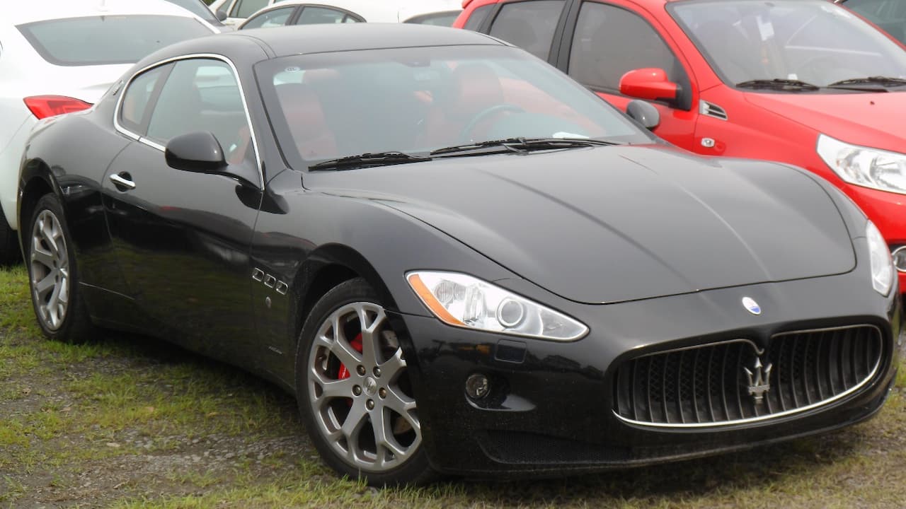 Black 2012 Maserati GranTurismo Base with distinctive trident grille parked on grass among other vehicles outdoors