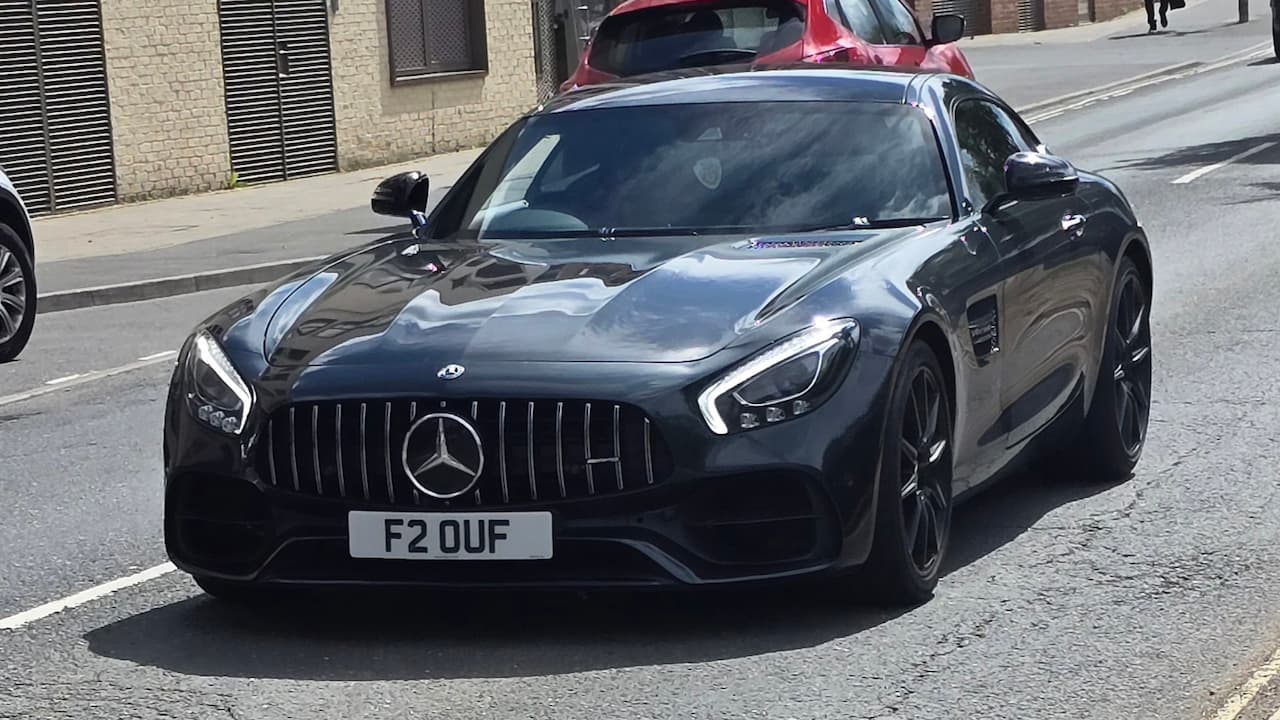 Black Mercedes-AMG GT with license plate "F2 OUF" parked on city street with Panamericana grille