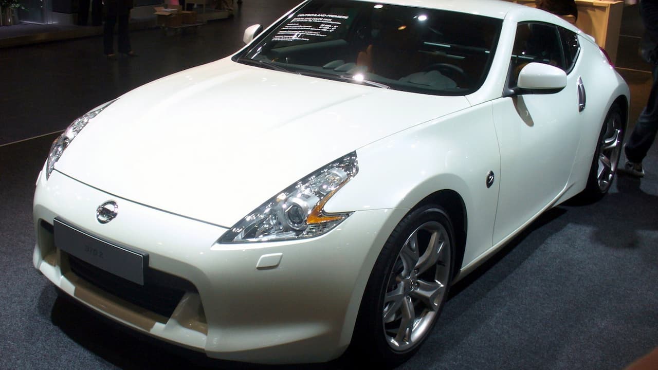 White Nissan 370Z with silver alloy wheels displayed indoors on dark floor under showroom lighting