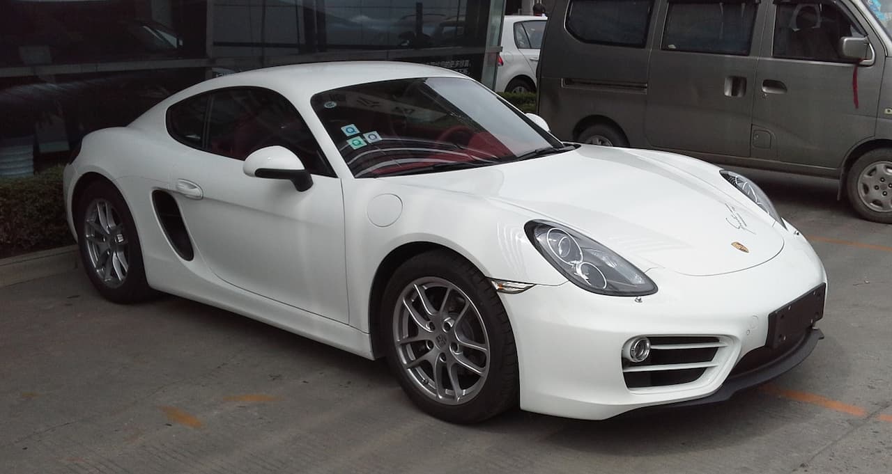 White 2014 Porsche Cayman parked in concrete garage with other vehicles including pickup truck nearby