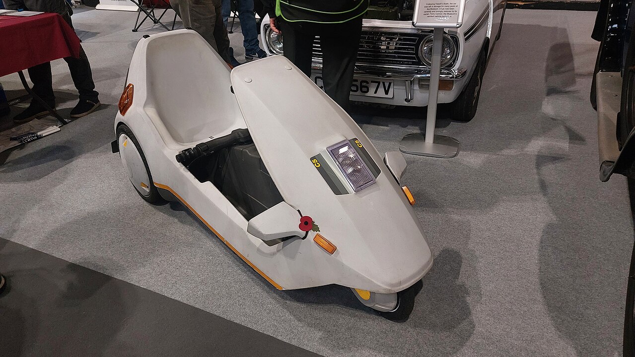 White Sinclair C5 electric vehicle with streamlined body and open cockpit displayed at indoor vehicle exhibition
