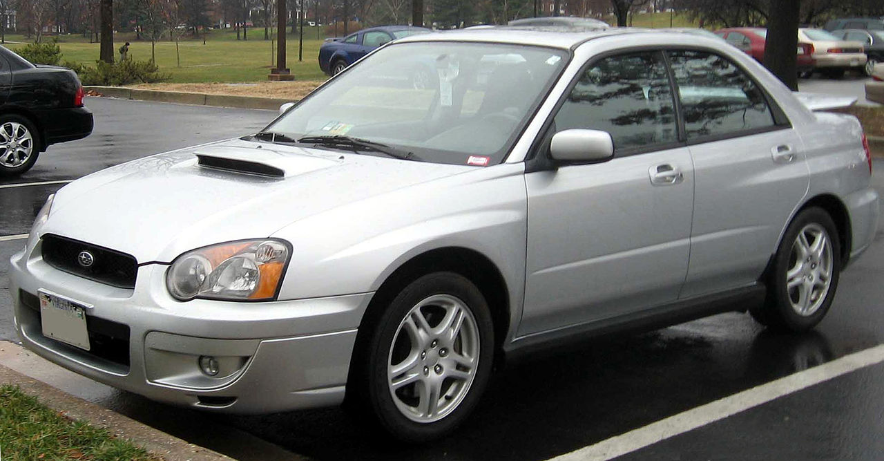 Silver 2004 Subaru WRX sedan parked in parking lot with hood scoop and five-spoke alloy wheels visible