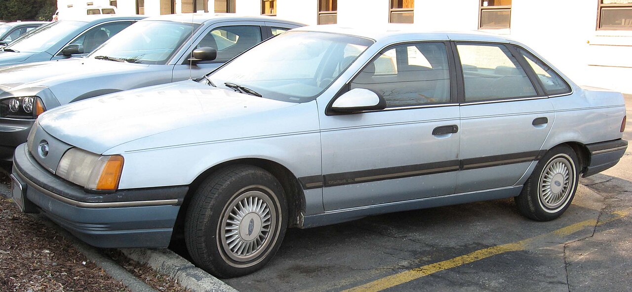 Grey 1986 Ford Taurus with distinctive aerodynamic styling parked on street near beige building