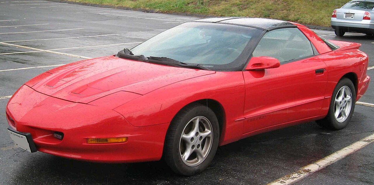 Red 1993 Pontiac Firebird sports car with T-top roof parked in parking lot with white lines
