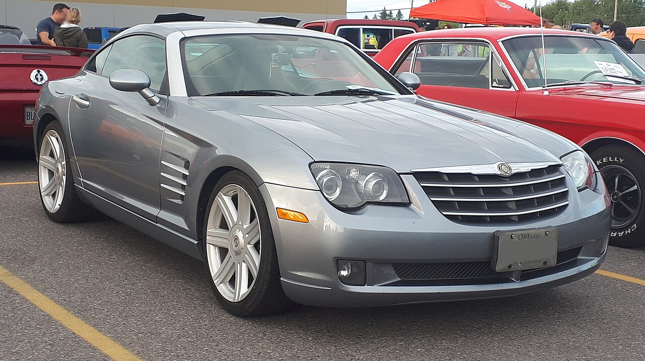 Silver 2004 Chrysler Crossfire sports car with distinctive side vents displayed at outdoor car show with spectators