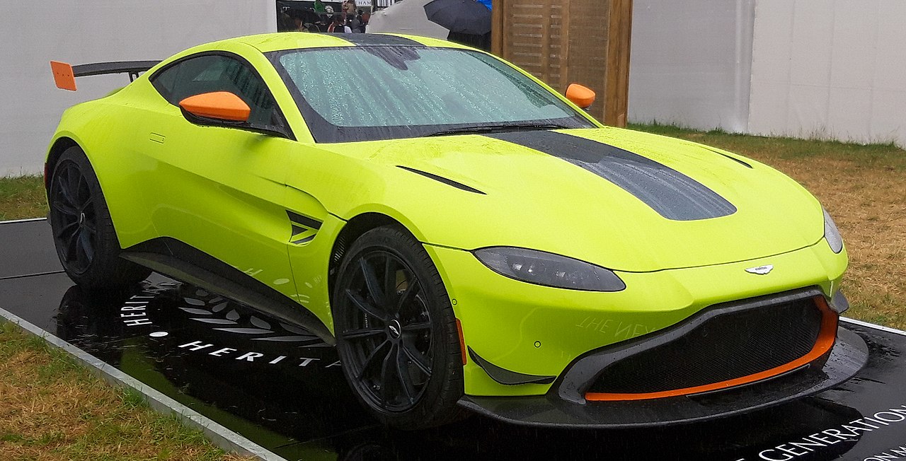 Aston Martin with Lime Essence paint and orange accents and large rear wing displayed on platform at event
