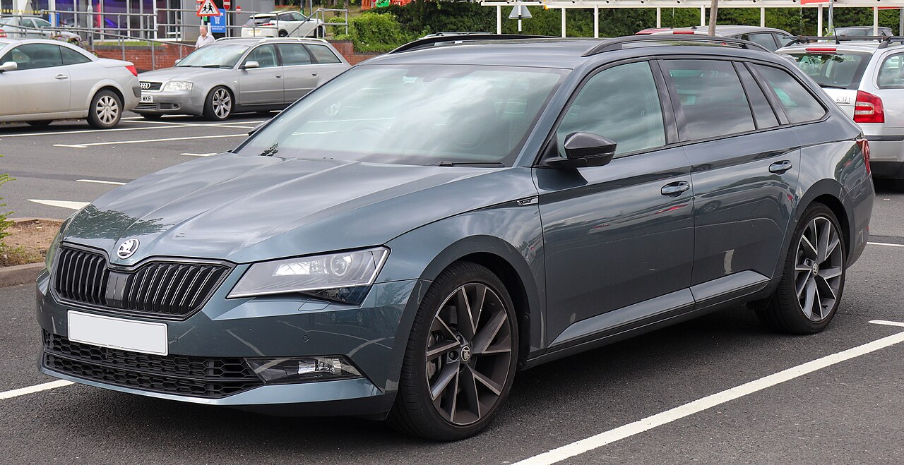 Dark gray Skoda Superb Estate parked in parking lot with distinctive front grille and alloy wheels