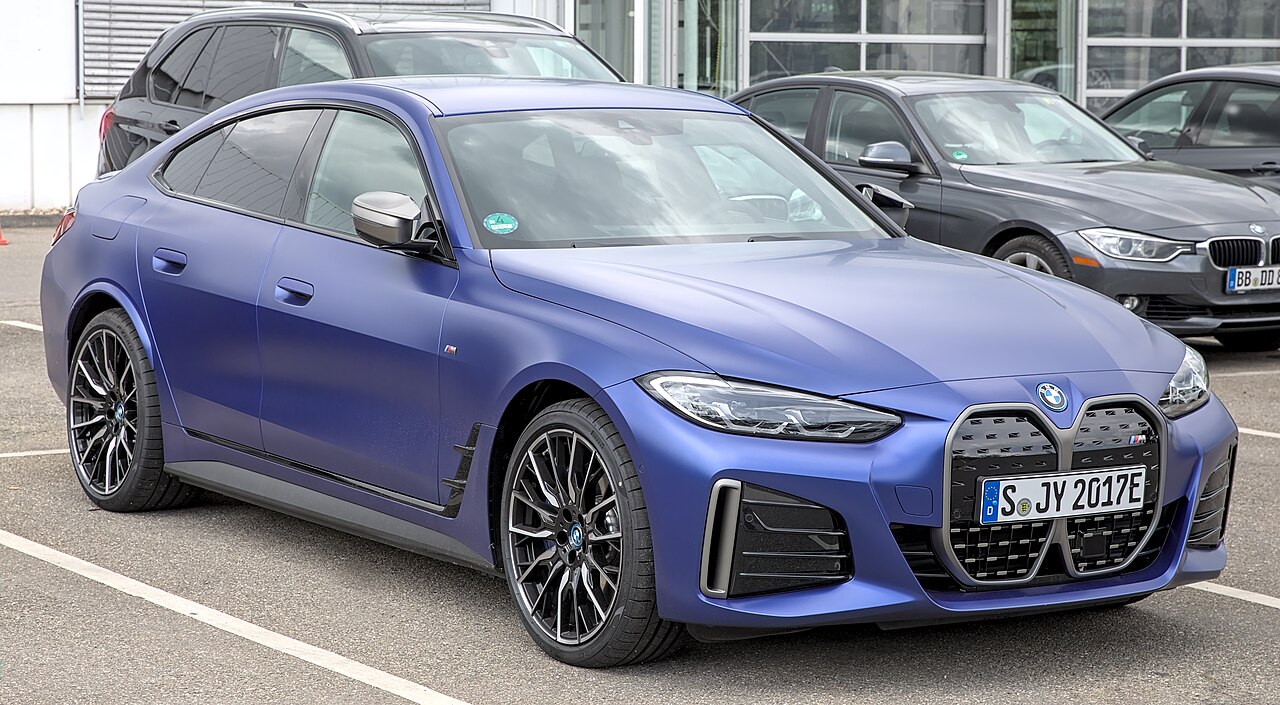 Blue BMW i4 M50 electric vehicle with distinctive kidney grille parked in dealership lot among other vehicles