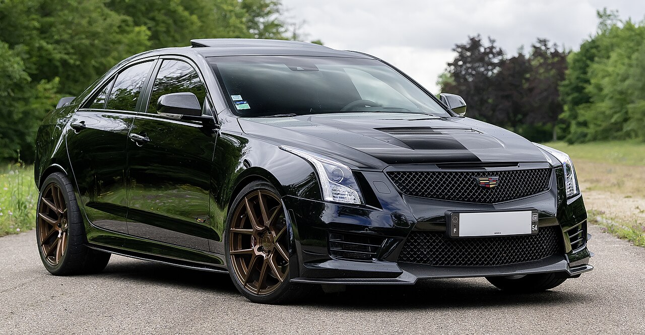 Black Cadillac ATS-V with bronze wheels and aggressive bodykit parked on rural road near trees