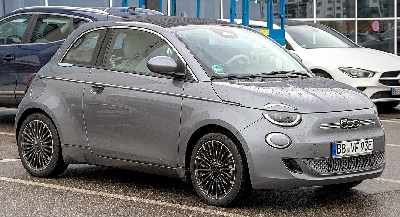 Gray Fiat 500e electric car with multi-spoke alloy wheels parked in dealership lot with other vehicles visible
