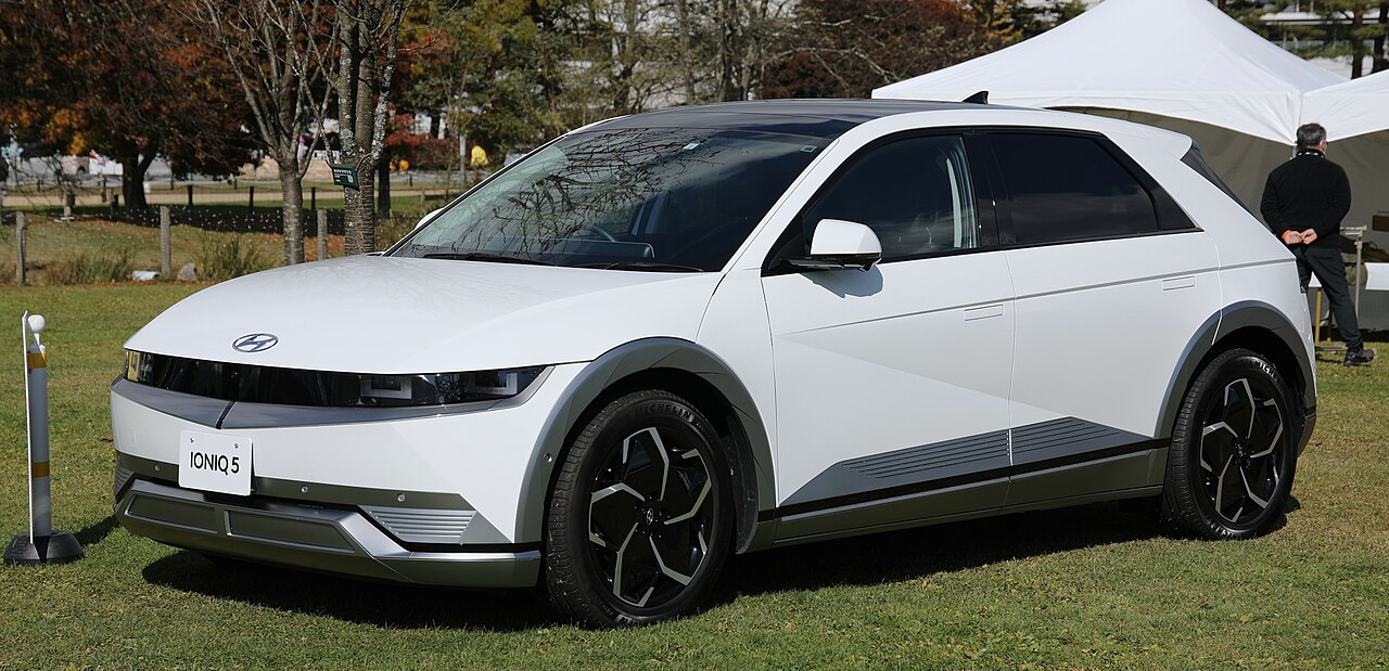 White Hyundai Ioniq 5 electric SUV with distinctive pixel LED headlights and aerodynamic design displayed on grass at outdoor event