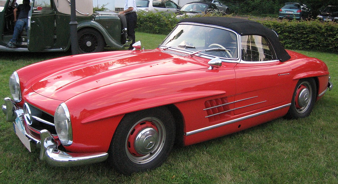 Red Mercedes-Benz 300 SL with black soft top parked on grass at classic car show