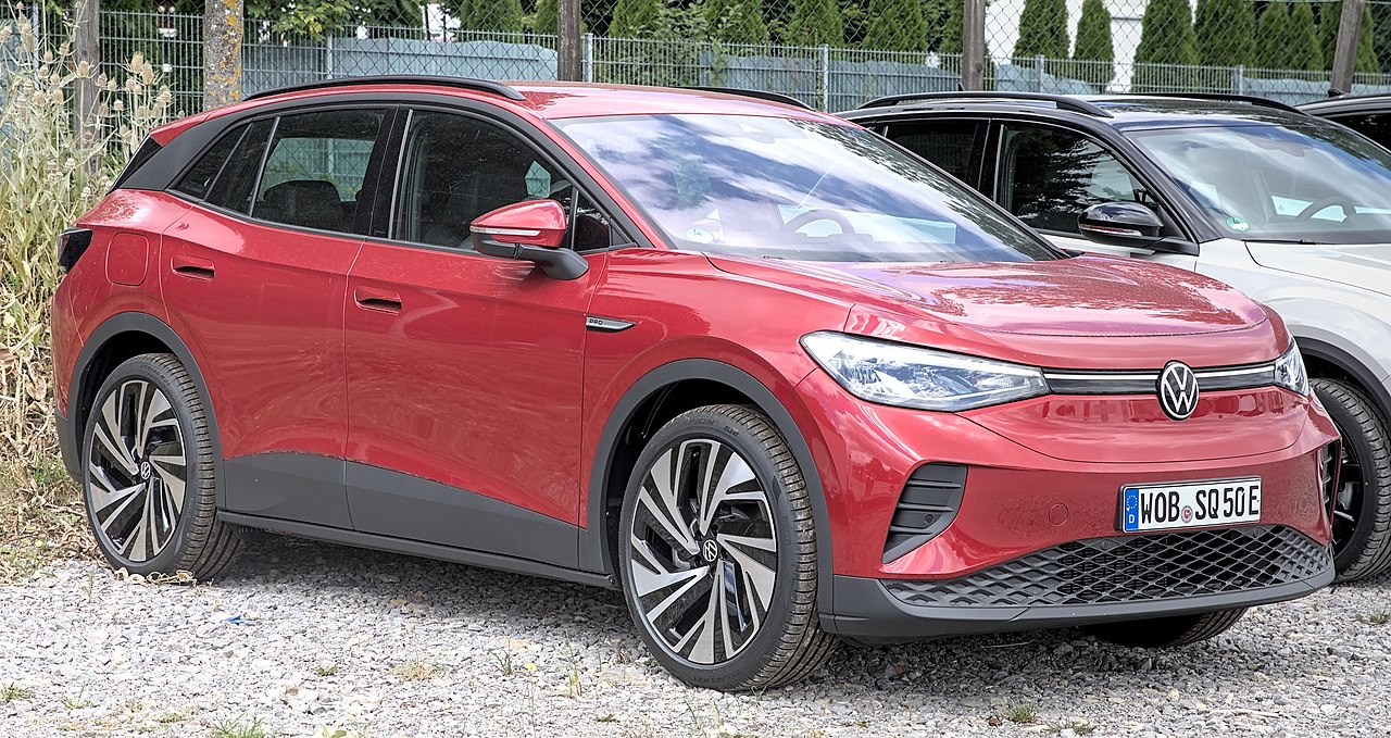 Red Volkswagen ID.4 electric SUV with distinctive LED headlights and large alloy wheels parked on gravel surface