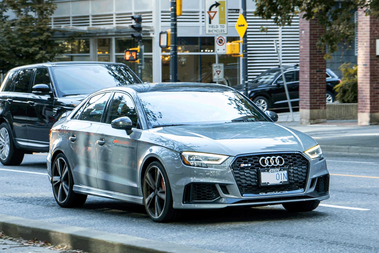 Silver Audi RS3 8V driving on wet city street with traffic lights and modern buildings in background