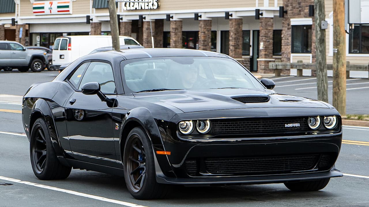 Black Dodge Challenger Scat Pack muscle car with widebody kit and dual headlights parked on street near commercial buildings