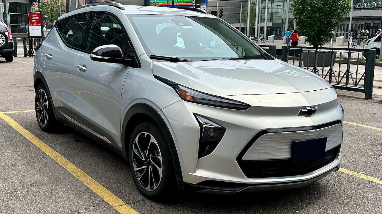 Silver Chevrolet Bolt EUV parked on street with modern styling, alloy wheels, and urban commercial buildings behind