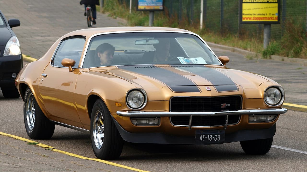 Gold 1971 Chevrolet Camaro Pro Touring with black racing stripes driving on street with cyclist in background