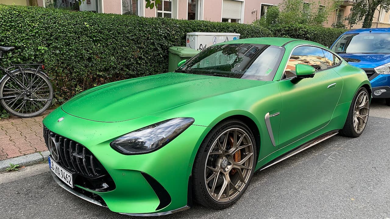 Bright green Mercedes-Benz AMG GT sports car with aggressive styling parked on residential street near apartment buildings