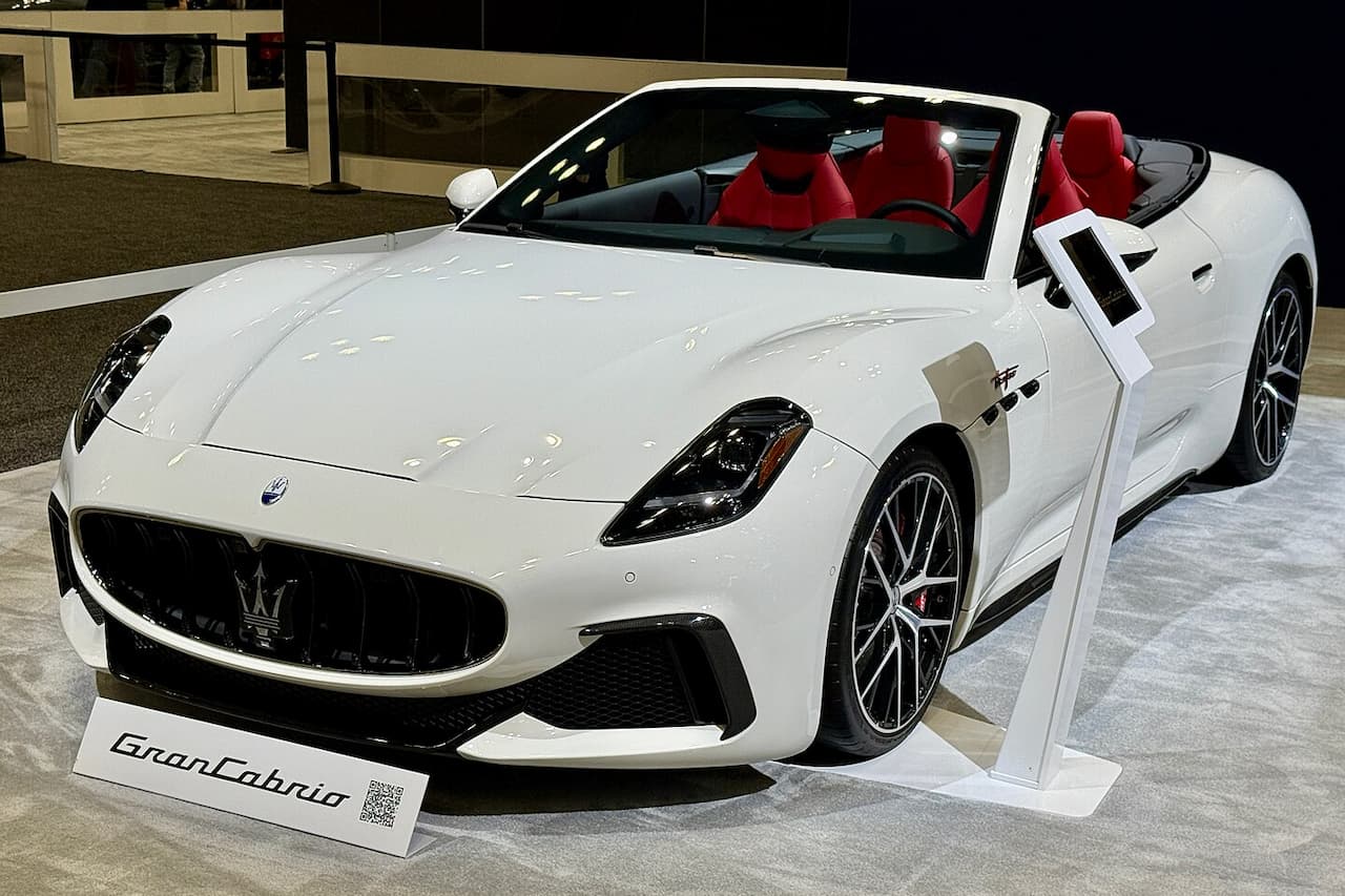 White Maserati GranCabrio Folgore with red interior displayed on white platform in modern showroom with nameplate