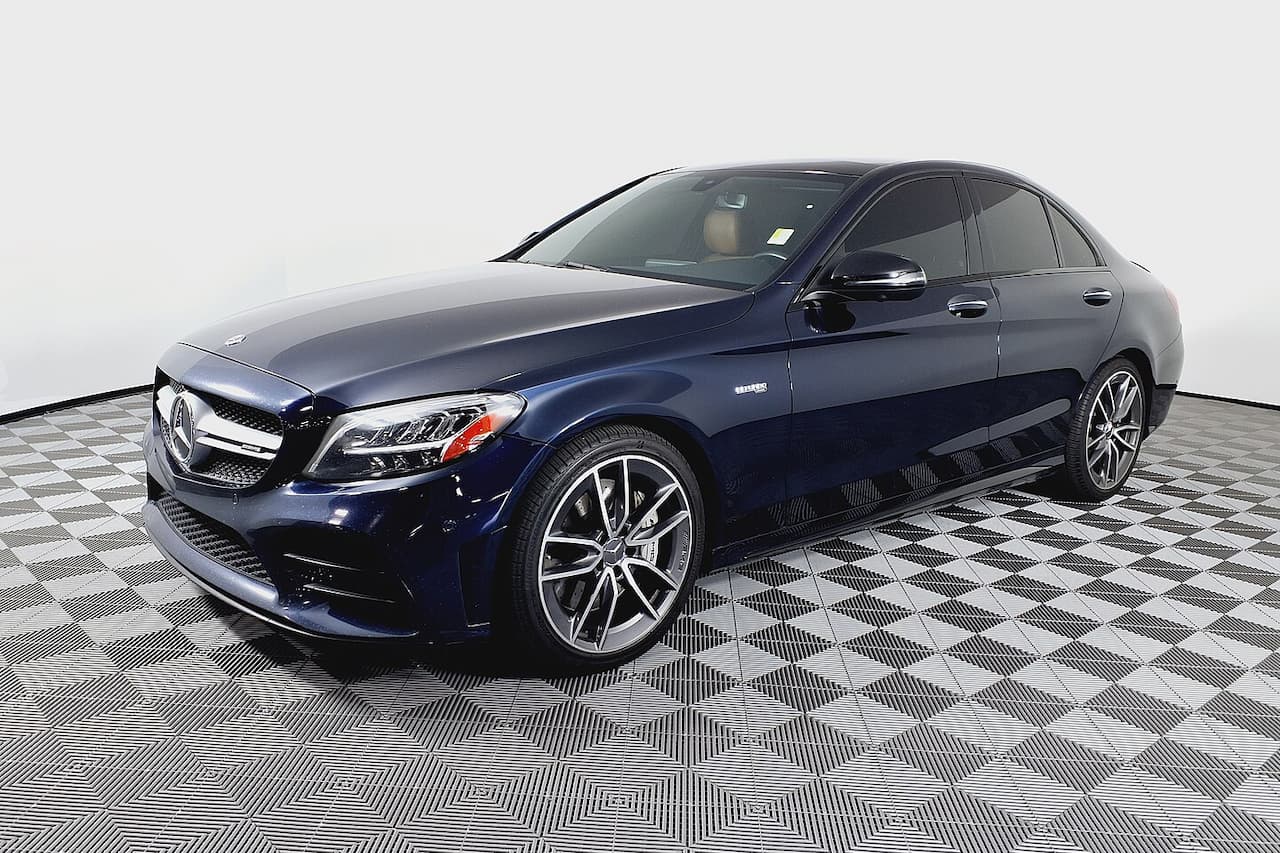 Dark blue Mercedes-AMG C43 with AMG wheels parked on checkered showroom floor against white background