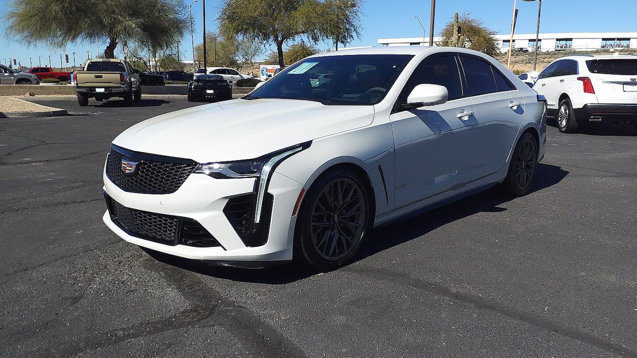 White Cadillac CT4-V Blackwing performance sedan with black wheels and aggressive styling parked in parking lot with other vehicles