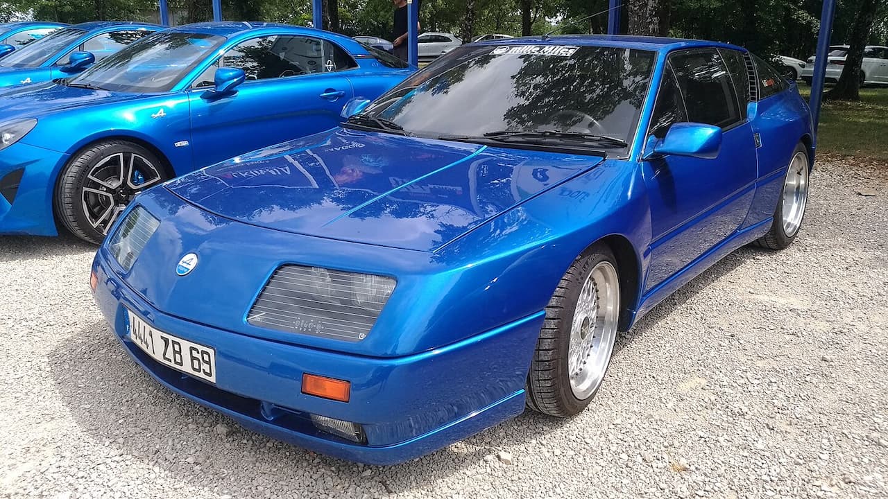 Blue Alpine GTA sports car with distinctive wedge design parked at car show with other vehicles nearby