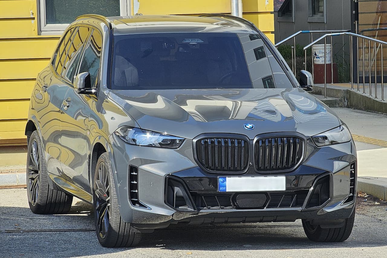 Gray BMW X5 hybrid with distinctive kidney grille and LED headlights parked on street with yellow building background