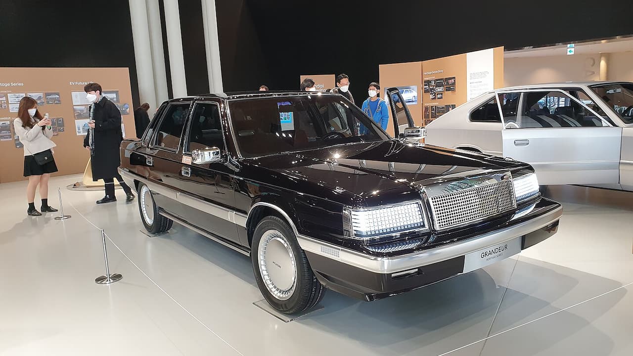 Black Hyundai Heritage Series Grandeur luxury sedan with white wall tires displayed in museum with visitors and exhibit panels