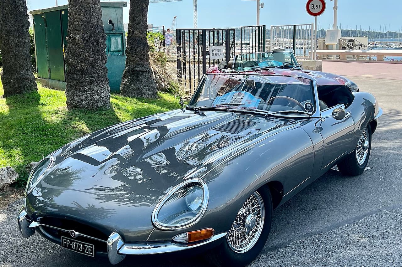 Grey Jaguar E-Type Zero with wire wheels parked on street near marina with boats and palm trees