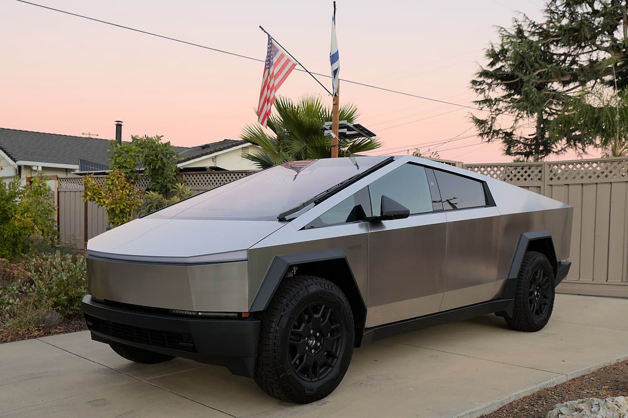 Silver Tesla Cybertruck parked on concrete driveway in residential area with angular stainless steel body and distinctive futuristic design