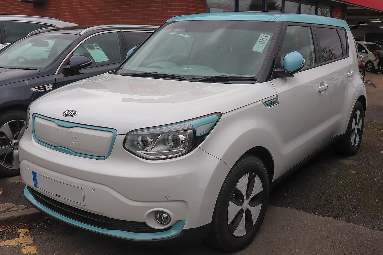 White Kia Soul EV with turquoise accent trim parked at dealership, featuring distinctive boxy design and electric vehicle styling cues