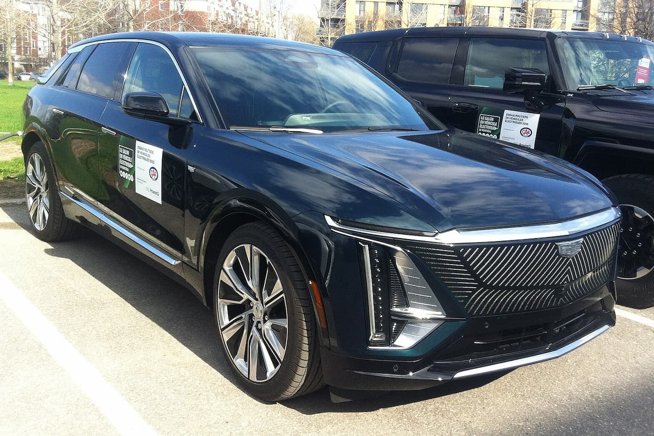 Black 2025 Cadillac LYRIQ electric SUV with distinctive grille and LED lights parked in lot with buildings behind