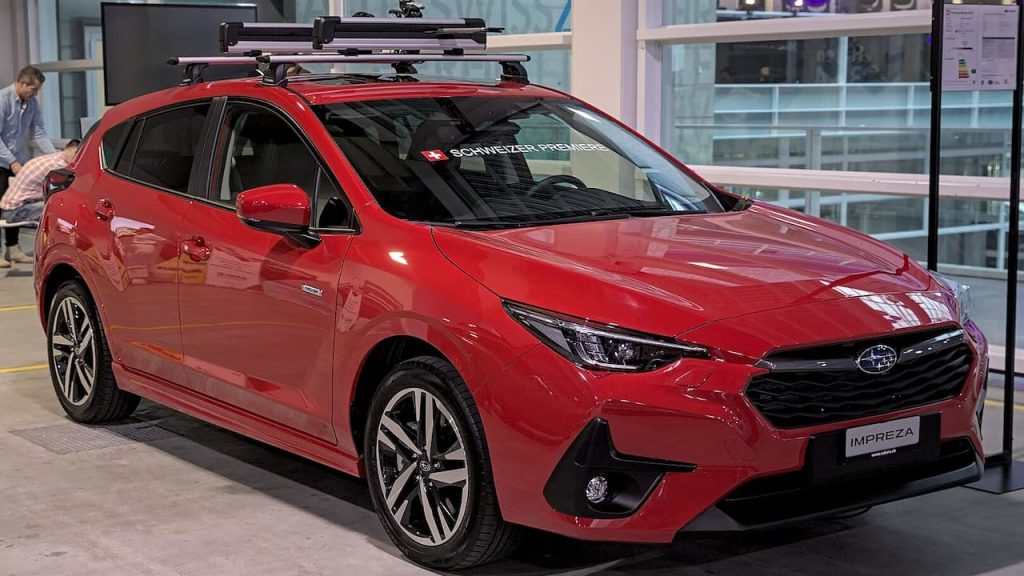 Red 2023 Subaru Impreza with roof rack displayed in dealership showroom with "IMPREZA" nameplate visible