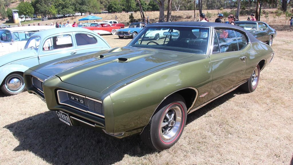 Olive green 1968 Pontiac GTO Endura-Delete muscle car displayed at classic car show with other vintage automobiles and spectators