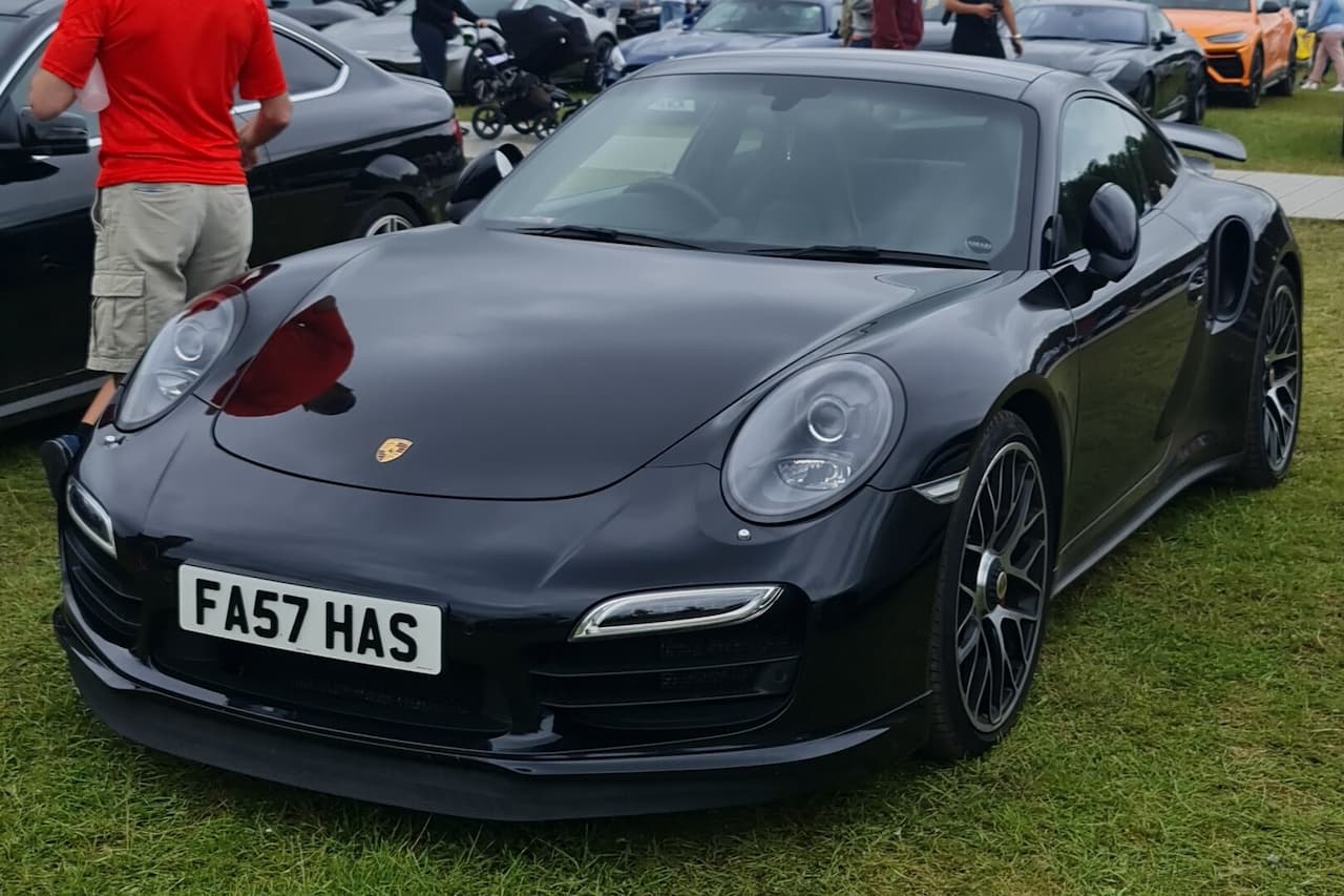 Black Porsche 911 Turbo with UK license plate parked on grass at outdoor car show event