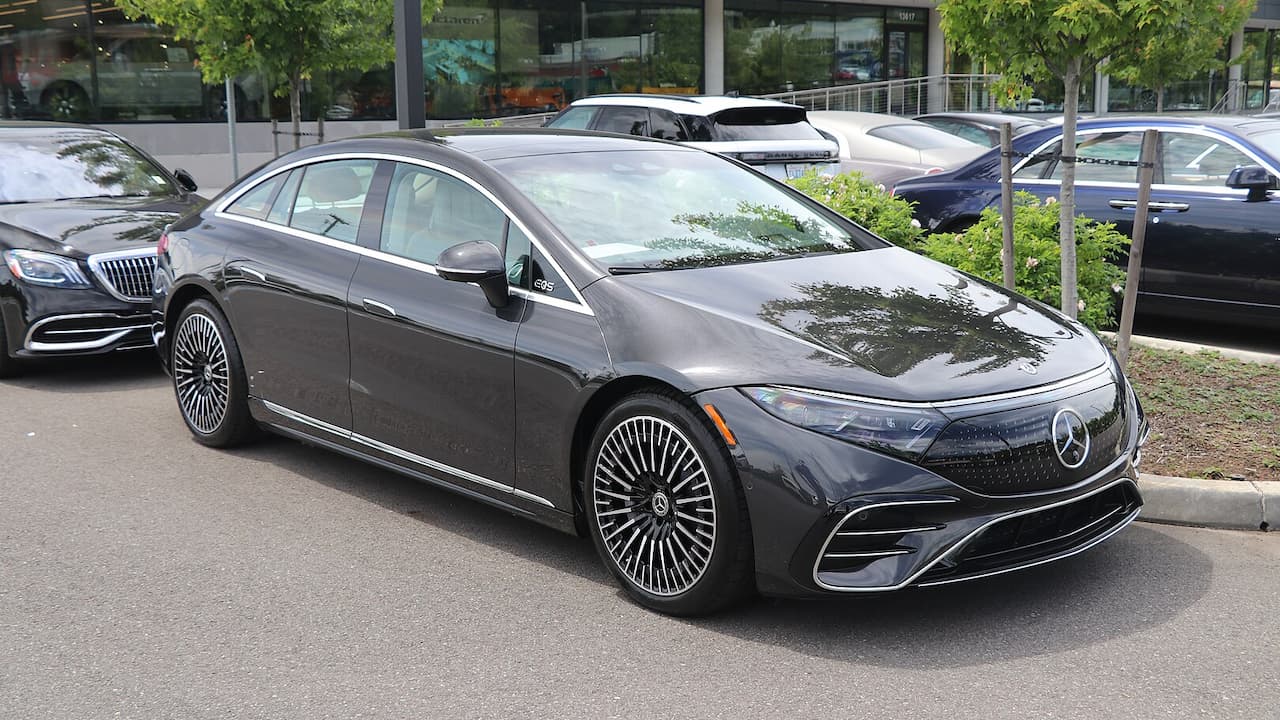 Dark gray Mercedes-Benz EQS 580 luxury electric vehcle with distinctive wheels parked in urban setting with other vehicles