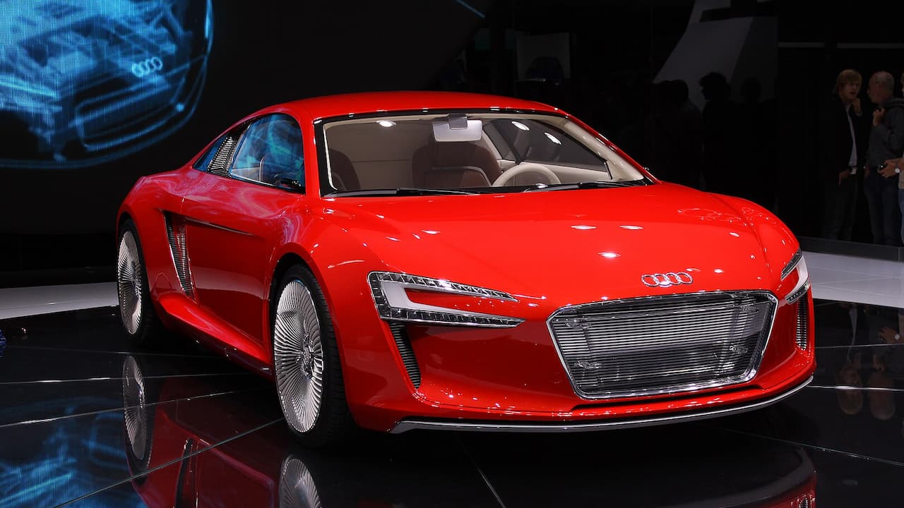 Red Audi e-tron displayed on black reflective floor at auto show with LED lights and futuristic design