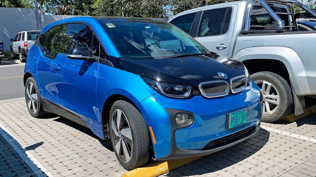 Bright blue BMW i3 electric car parked on brick pavement with distinctive kidney grille, aerodynamic wheels, and vehicles behind